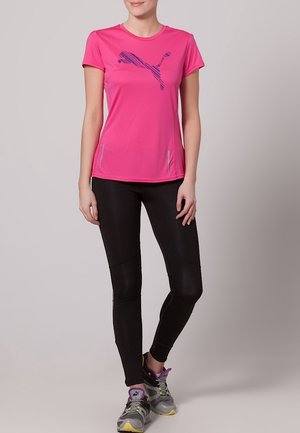 T-shirt sportivo rosa brillante con logo Puma blu, abbinato a leggings neri con pannelli laterali, indossati con scarpe da corsa grigie e gialle.