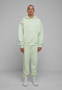 Sudadera verde menta clara con bolsillo canguro, puños acanalados, y pantalones jogger a juego con puños elásticos. Combinada con zapatillas blancas.