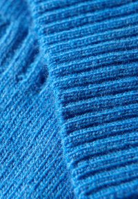 Blau gestrickter Stoff mit einem strukturierten Rippenmuster, das glatte und flauschige Fasern zeigt und die Tiefe und Lebhaftigkeit der Farbe hervorhebt.