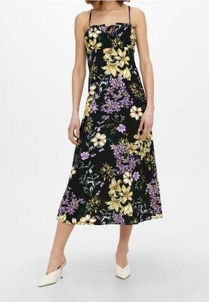 Czarna sukienka midi z żółto-fioletowym kwiatowym nadrukiem, cienkimi ramiączkami i marszczonym dekoltem, noszona z białymi czółenkami z ostrym noskiem.