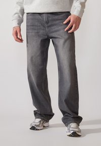Dark grey denim jeans with a straight-leg fit, visible stitching, and standard five-pocket design, paired with athletic shoes.