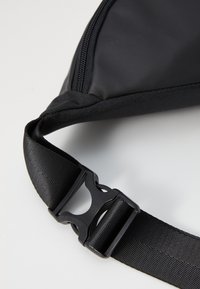 Sangle de sac noir avec une boucle en plastique et une fermeture éclair, capturant un gros plan du mécanisme de fixation et des bords du sac.