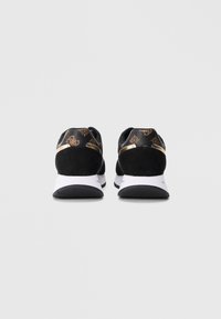 Para czarnych sneakersów ze złotymi akcentami i wzorzystym piętą, widziana od tyłu na jednolitym białym tle.