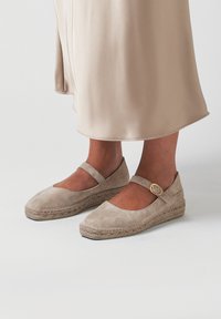 Espadrilles de ante color beige con punta redondeada, tira en el tobillo y hebilla en tono dorado. Suela envuelta en yute y textura suave.