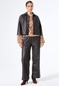 Bruine leren cropped blazer over een beige trui met een luipaardprint, gecombineerd met bijpassende bruine leren wijde pantalons en bruine hakken.