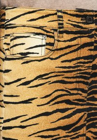 Pantalons en denim imprimé tigre avec une petite poche avant et un bouton noir de fermeture à la taille.
