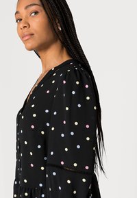 Vestido preto com bolinhas coloridas em rosa, azul e amarelo. O design inclui mangas bufantes e um decote em V.