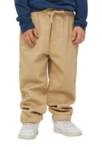 Beżowe spodnie cargo z elastycznym paskiem i sznurkiem do regulacji, z dwoma bocznymi kieszeniami i mankietami zwiniętymi na kostkach. Noszone z białymi sneakersami.