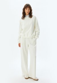 Sudadera blanca y pantalones a juego de tejido suave, con un ajuste holgado y piernas anchas. El conjunto no presenta patrones visibles ni elementos metálicos.