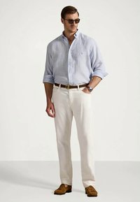 Lys blå stripete skjortebluse med knapper, hvite bukser, brunt belte og brune loafers. Modellen har på seg solbriller og klokke. Klassisk uformell antrekk.