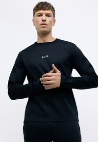 Camiseta negra de manga larga hecha de un tejido suave, con un cuello redondo y un pequeño logo blanco de "BOSS" en el pecho.