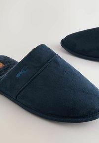 Navy blue slippers made of soft suede with a plush lining. Features an embroidered lobster logo and a closed-back design. Lightweight and flexible.