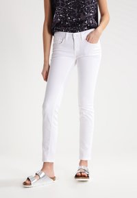 Jeans de mezclilla blanca con un corte slim, cinco bolsillos y un ligero estiramiento. Combinados con una blusa negra con un diseño de estampado de leopardo y sandalias plateadas.