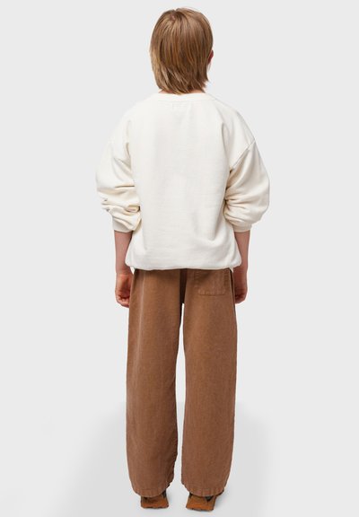 Sudadera crema con hombros caídos, combinada con pantalones de pierna ancha marrones que tienen un bolsillo trasero. Textura suave con un ajuste relajado.