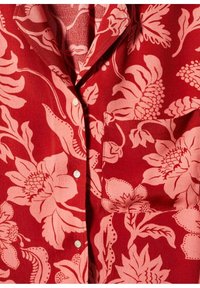 Camicia floreale rossa con motivo botanico rosa chiaro, chiusura a bottone e taschino sul petto, realizzata in tessuto morbido con una texture liscia.