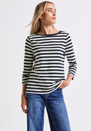 Randig långärmad topp i marinblått och krämigt, med rundad halsringning och avslappnad passform. Bärs med blekta blå vida jeans.