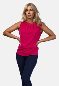 Fuksjowy top bez rękawów z plisowanym dekoltem, w zestawie z ciemnoniebieskimi spodniami w kropki. Gładki materiał i dopasowany krój. Brak widocznych elementów metalowych.