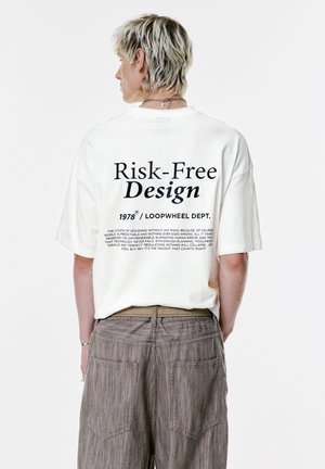 Weißes, übergroßes T-Shirt mit schwarzem Text auf dem Rücken. Kombiniert mit strukturierten, taubfarbenen Hosen. Schlichtes und minimalistischem Design.