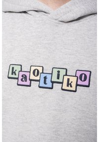 Sweat à capuche gris avec des lettres en blocs colorés formant le mot "kaotiko" sur la poitrine dans des carrés pastel vert, violet, beige et bleu.