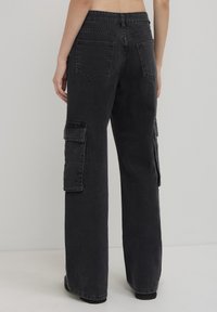 Pantaloni cargo neri con una vestibilità rilassata, dotati di tasche laterali e dettagli con borchie. Realizzati in denim, presentano una texture spazzolata e dettagli cuciti.