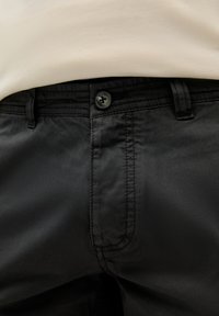 Pantalones de algodón negros con textura suave, que cuentan con cierre de botón, pasadores para cinturón y detalles de costura sutiles.