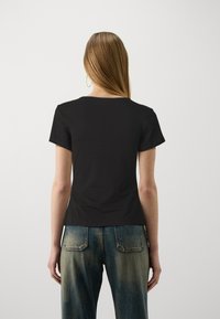 Schwarzes T-Shirt mit kurzen Ärmeln und rundem Halsausschnitt, aus glattem Baumwollstoff. Kombiniert mit ausgewaschenen, blauem, hoch tailliertem Jeans, die über Gesäßtaschen verfügen.