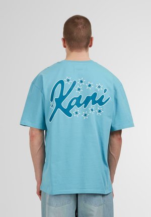 A relaxed-fit, light blue cotton t-shirt featuring a large white and teal graphic with "Kani" and star designs on the back.
