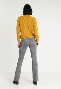 Hořčicově žlutý pletený svetr se vzorem cikcak, kombinovaný se šedými rozšířenými kalhotami se vzorem a černými botami na platformě.