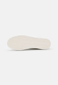 Semelle de baskets blanches avec un motif en chevrons texturé, présentant un bord lisse et des détails subtils le long du périmètre.