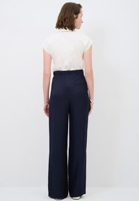 Haut crème à manches courtes associé à un pantalon large bleu marine. Le pantalon est doté d'une poche arrière unique et de passants de ceinture. Texture de tissu lisse.