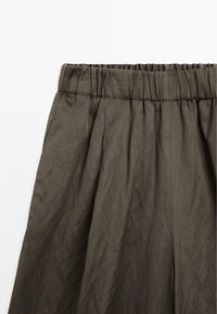 Elastische taillebandrok van donkergroene stof. Kenmerkt zich door plooien en een gladde textuur, met zijzakken die functionaliteit toevoegen.