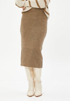 Strick-Bleistiftrock in Beige mit geripptem Saum. Kombiniert mit glänzenden weißen Stiefeln bis zum Knie. Minimalistisches Design mit weicher Textur.