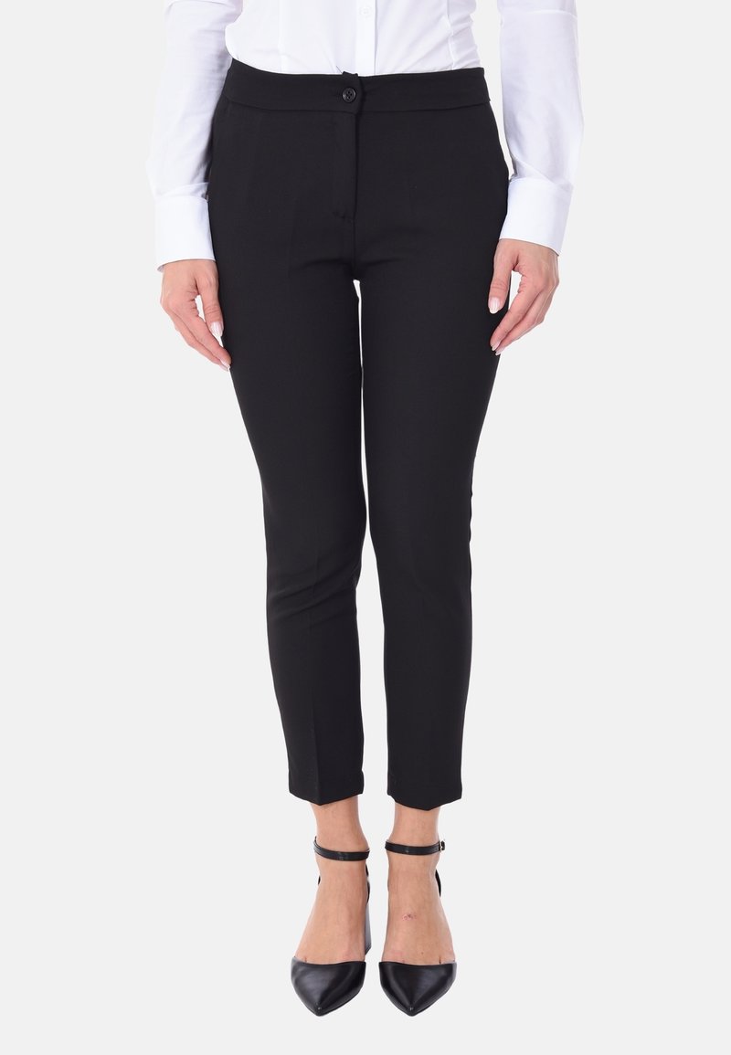 Pantaloni neri su misura con una vestibilità slim, caratterizzati da un tessuto liscio, chiusura frontale con bottone e taglio alla caviglia. Abbinati a tacchi a punta.