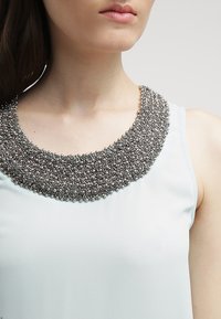 Top senza maniche azzurro chiaro con un colletto di perline silver texture, caratterizzato da una forma rotonda e un tessuto morbido, con un'attenzione particolare ai dettagli del decolletè.