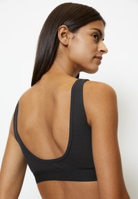 Brassiere sportivo nero a coste con design a schiena bassa, spalline larghe e texture liscia. Senza accessori o imbottiture visibili. Stile minimalista.
