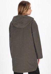 Olivengrøn hættetrøje med løs pasform, glat stof og sideslidser for nem bevægelse. Enkel syning og minimal detaljer.