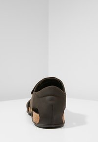 Brown leather sandal with cork accents, open back design, adjustable strap, and textured surface. Features cutouts for breathability.