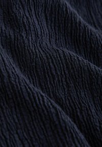 Tissu bleu marine foncé avec un motif texturé froissé de crêtes verticales créant de doux plis et des ombres sur la surface.