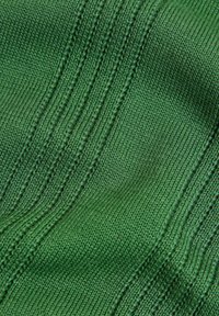 Nahaufnahme eines grünen Strickstoffs mit vertikalen, gerippten und strukturierten Stichen, die ein wellenförmiges Muster bilden.