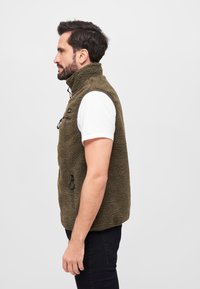 Olivgrüne Fleece-Weste mit hohem Kragen, durchgehendem Reißverschluss und seitlicher Tasche. Besitzt eine weiche, strukturierte Oberfläche und einen lässigen Schnitt.