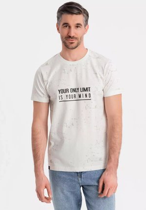 Camiseta blanca con un patrón moteado y texto negro que dice "TU ÚNICO LÍMITE ERES TÚ MENTE." Cuello redondo, mangas cortas, corte casual.