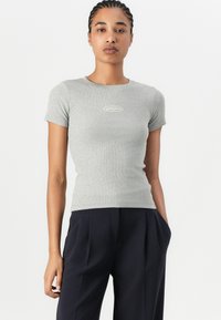 T-shirt grigia a maniche corte con costine, dal design aderente e un piccolo logo sul petto, abbinata a pantaloni scuri e morbidi.