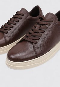 Zapatillas de cuero marrón con una superficie texturizada, con puntera redonda, cordones a tono y una suela de goma blanca contrastante.