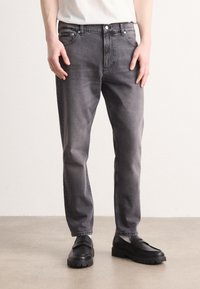 Grå denimjeans med rak benpassform, fem fickor och kontrasterande sömmar, matchade med svarta loafers med tjocka sulor.