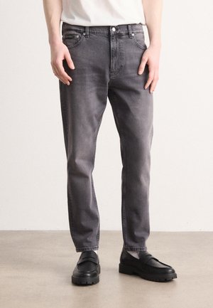 Jeans de mezclilla gris con corte recto, cinco bolsillos y costuras en contraste, combinados con mocasines negros de suela gruesa.