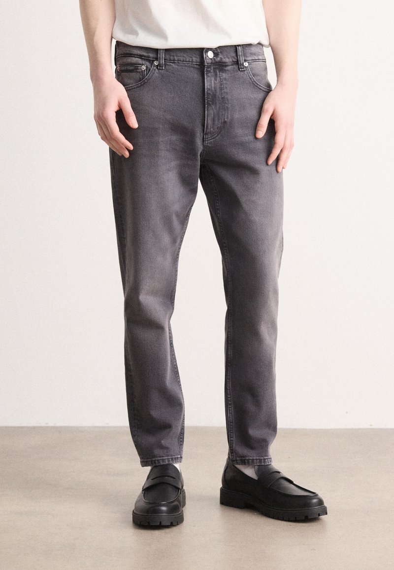 Grå denimjeans med rak benpassform, fem fickor och kontrasterande sömmar, matchade med svarta loafers med tjocka sulor.