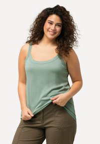 Light green tank top with a scoop neckline and wide straps. Soft fabric with a slightly loose fit, paired with olive green pants.