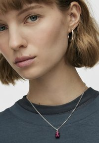 Collar de cadena de plata con un colgante de cuentas rosa texturizado. El modelo lleva un sudadera gris oscuro con un cuello acanalado.