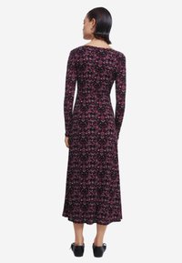 Langärmliges, schwarzes Kleid mit Blumenmuster, das einen taillierten Oberteil und einen ausgestellten Rock hat. Glatte Stoffqualität mit Rundhalsausschnitt, endet unterhalb des Knies.