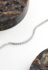 Söljd pärlkedja liggande över två cirkulära, mörka stenskivor med gulddetaljer och texturerade ytor.